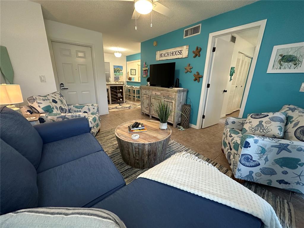 A living room features a blue sofa, patterned armchairs, a wooden coffee table, and teal walls — 6825 STONES THROW CIRCLE N UNIT 1107, ST PETERSBURG, FL