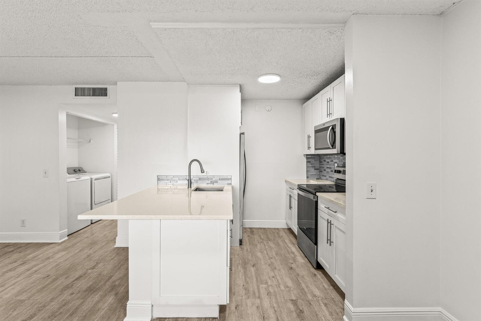 A kitchen features white cabinets, stainless steel appliances, a quartz island, and light wood flooring — 507 Meadows Circle, Boynton Beach FL 33436, BOYNTON BEACH, FL