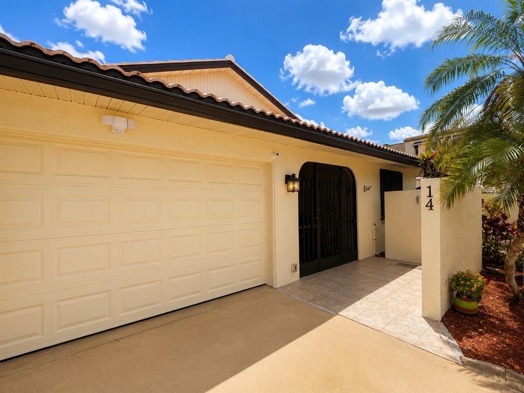 The exterior of a house features a beige garage door, a gated entryway, and address 14 — 14 IDLE SANDS DRIVE, VENICE, FL