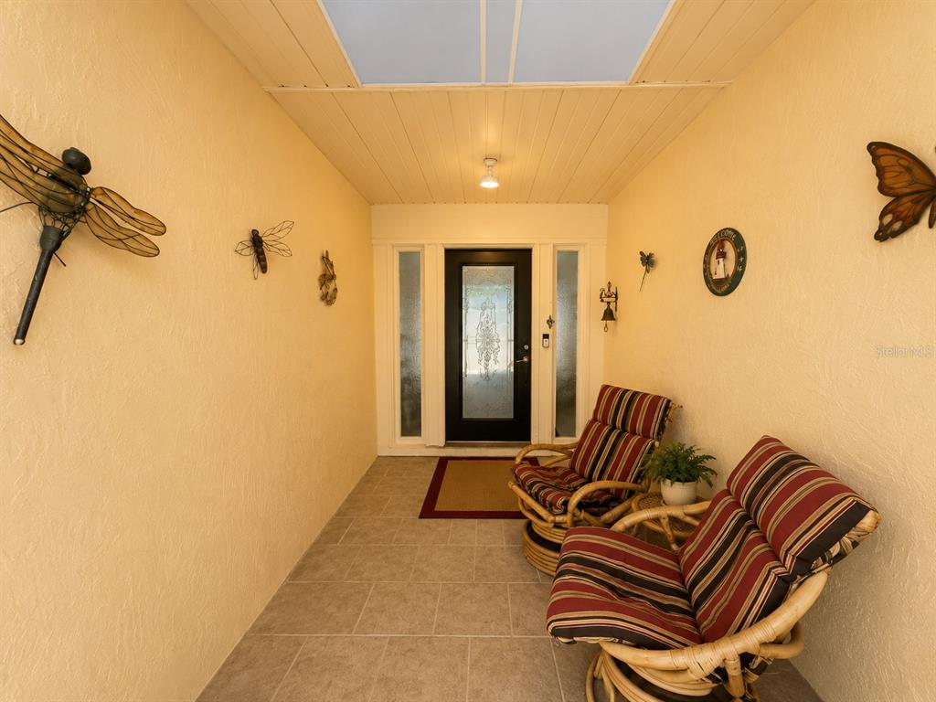 A covered entryway features tiled flooring, two wicker chairs, and wall-mounted insect decorations — 14 IDLE SANDS DRIVE, VENICE, FL