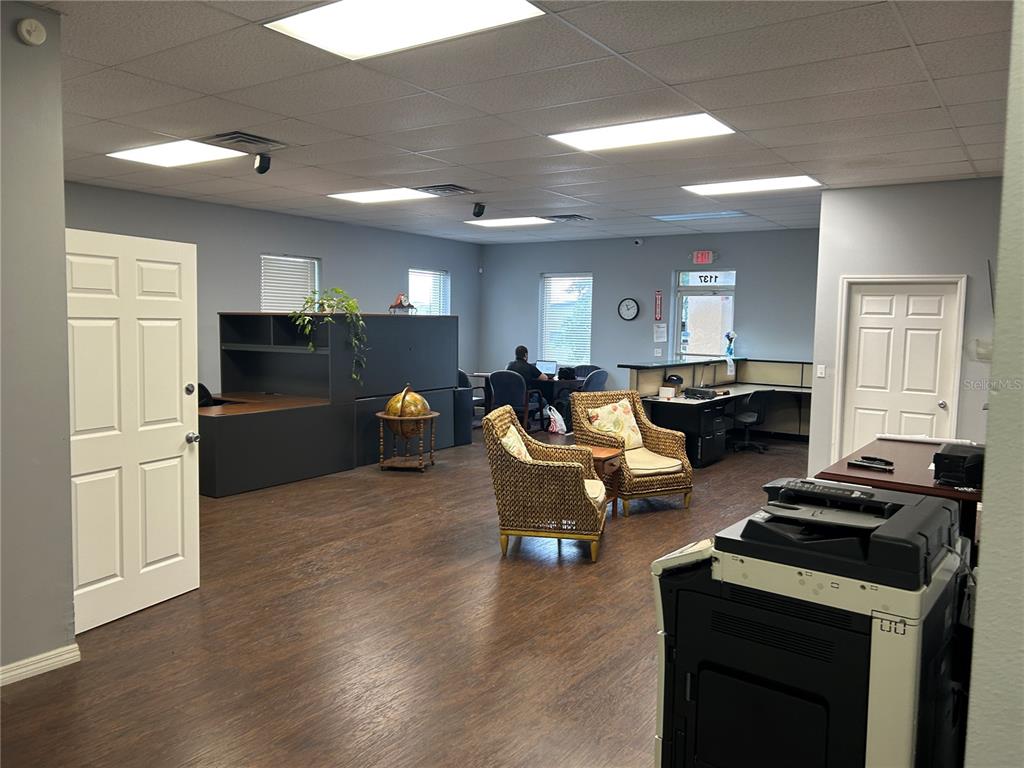 An office space features wood-look flooring, wicker chairs, a desk area, and a large printer — 1137 SW 7TH ROAD, OCALA, FL