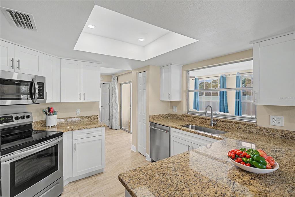 A kitchen features white cabinets, granite countertops, stainless steel appliances, and a recessed ceiling light — 9136 TIARA COURT, NEW PORT RICHEY, FL