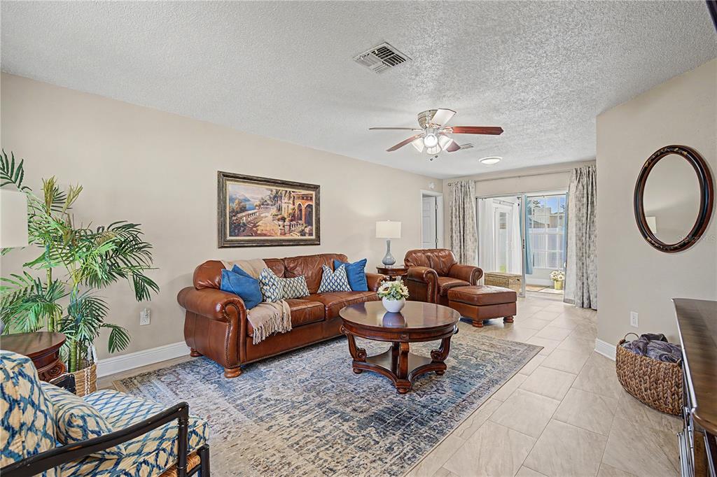 A living room features a leather sofa, a round coffee table, and tile flooring — 9136 TIARA COURT, NEW PORT RICHEY, FL