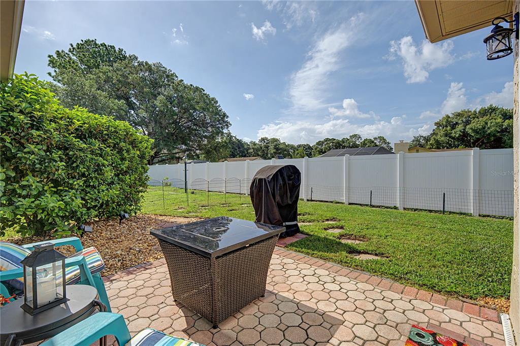 A paved patio overlooks a grassy backyard enclosed by a white vinyl privacy fence — 9136 TIARA COURT, NEW PORT RICHEY, FL