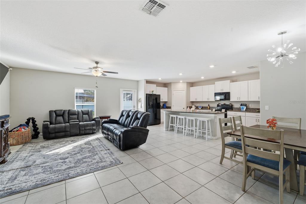 An open-concept living room and kitchen featuring tile floors, white cabinetry, and dark furniture — 2007 SEA SALT COURT, RUSKIN, FL
