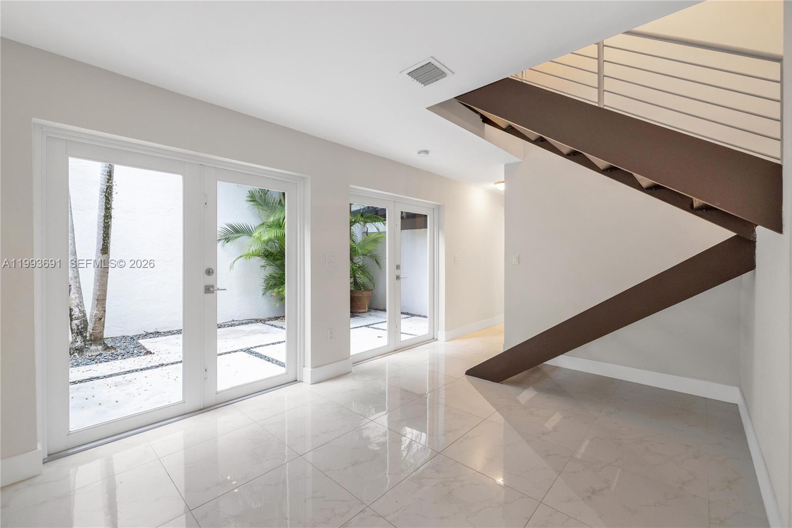 A modern entryway features white tile floors, glass doors to a courtyard, and a staircase — 3056 Shipping Ave # 2, Miami FL 33133, MIAMI, FL
