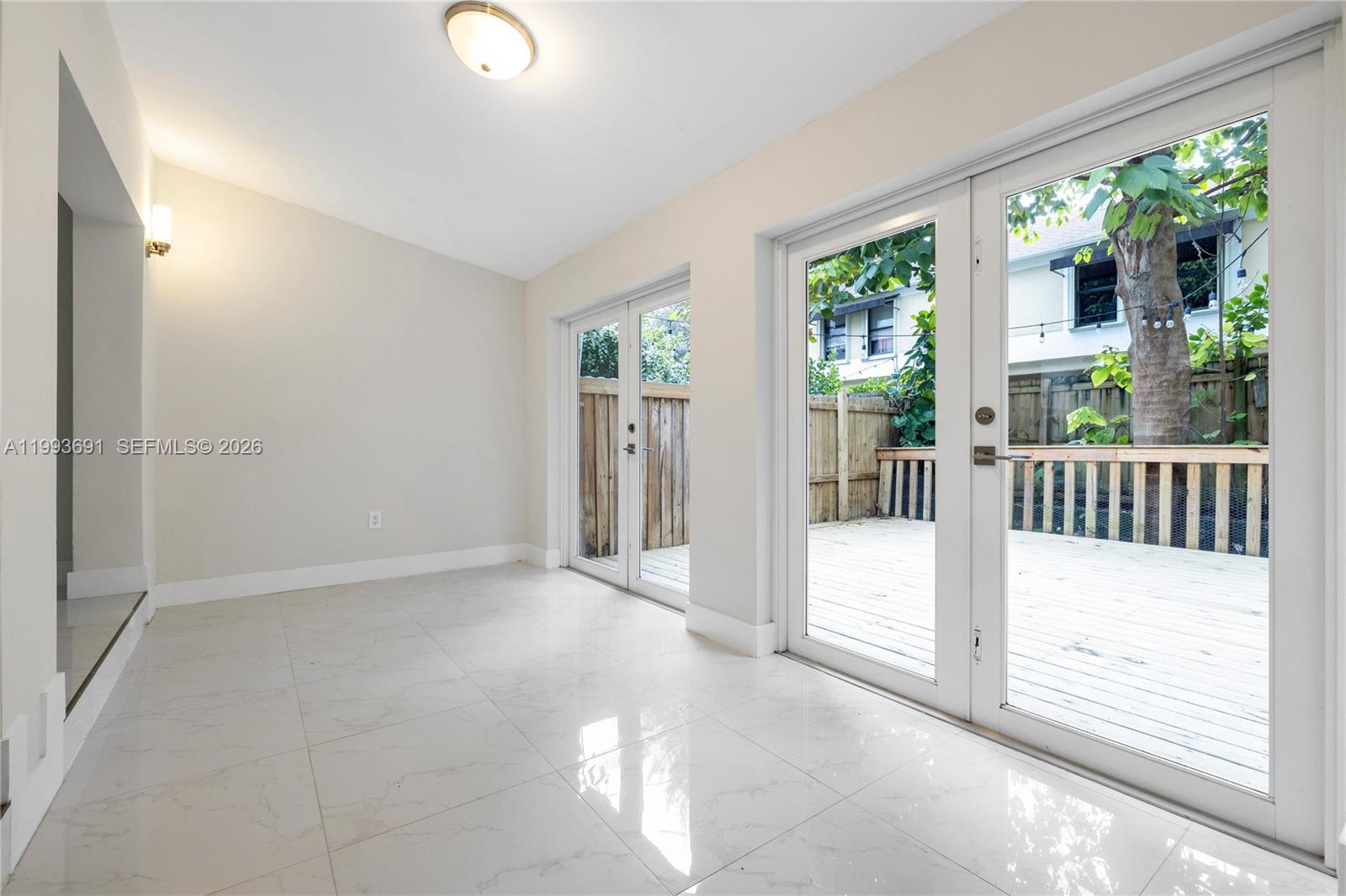 An empty room with white tile floors features two sets of glass doors leading outside — 3056 Shipping Ave # 2, Miami FL 33133, MIAMI, FL