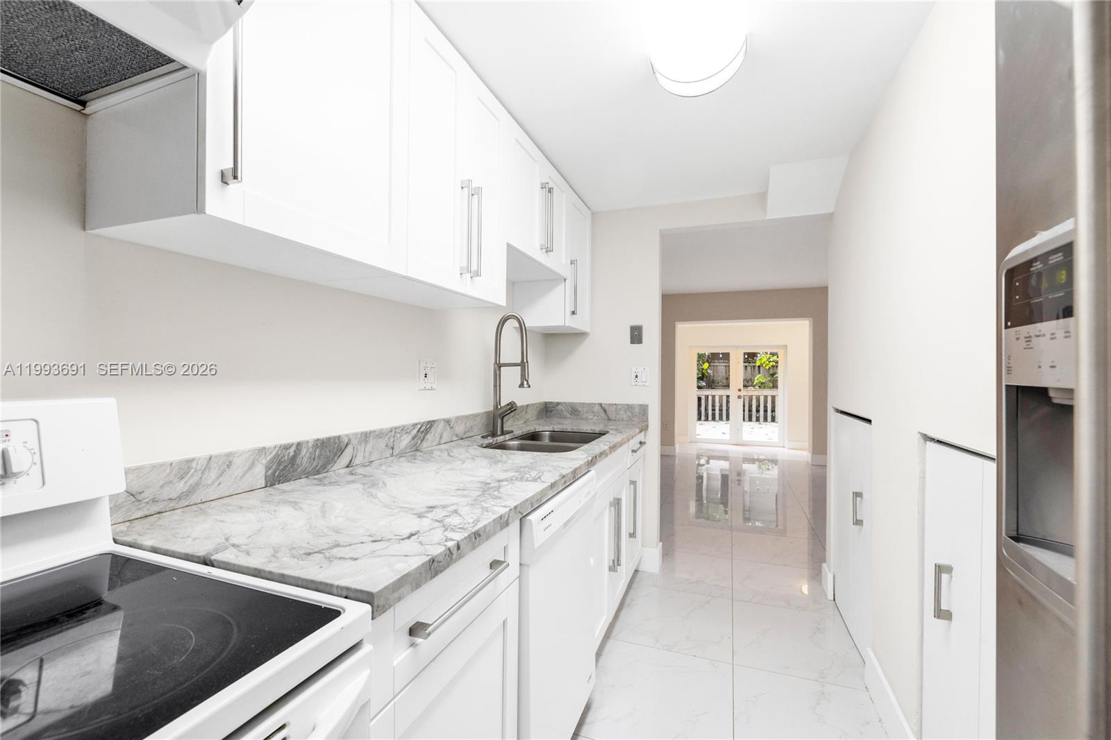A galley kitchen features white cabinets, marble-patterned countertops, and stainless steel appliances — 3056 Shipping Ave # 2, Miami FL 33133, MIAMI, FL