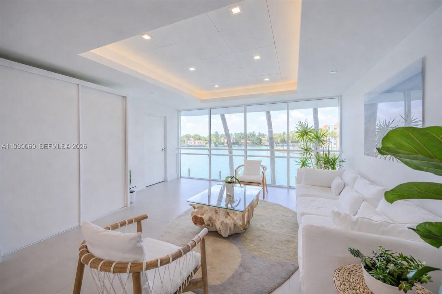 A bright living room features white furniture, a driftwood coffee table, and floor-to-ceiling waterfront windows — 5900 Collins Ave # 1405, Miami Beach FL 33140, MIAMI BEACH, FL