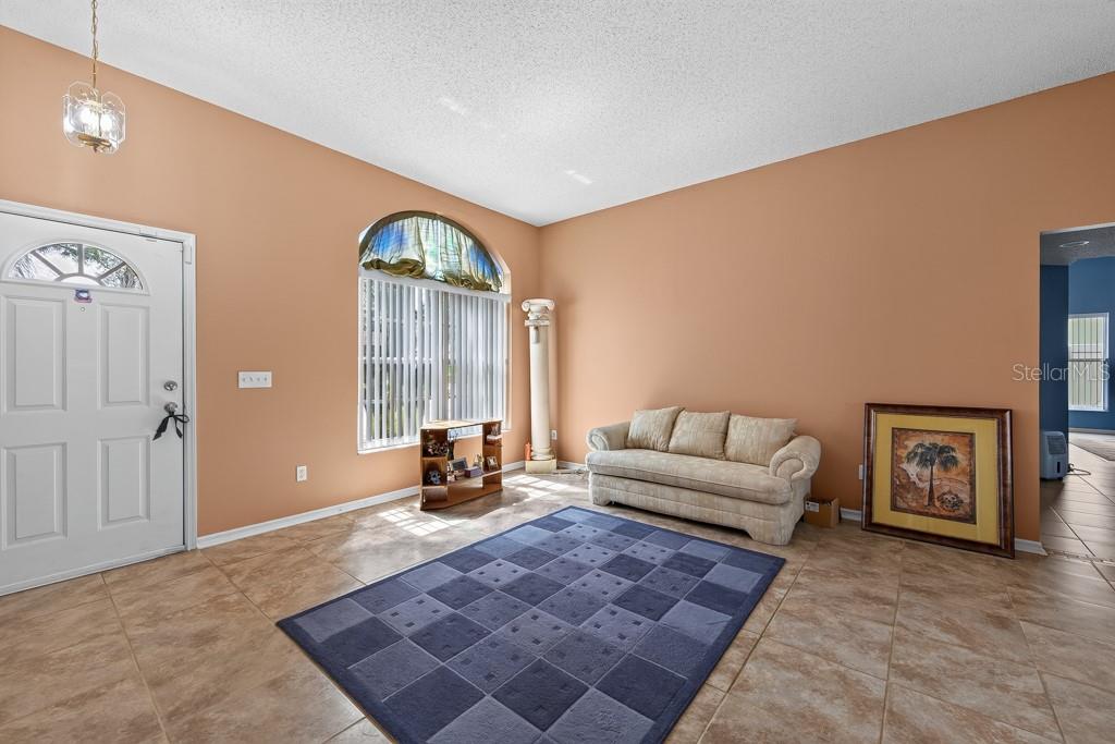 A living room with peach walls, tile flooring, a blue rug, and a beige sofa — 4609 OAK RIVER CIRCLE, VALRICO, FL