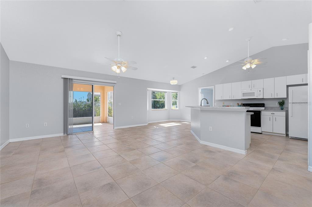 An open-concept living area features tile flooring, a kitchen with white cabinets, and sliding doors — 1053 BAY HARBOR DRIVE, ENGLEWOOD, FL
