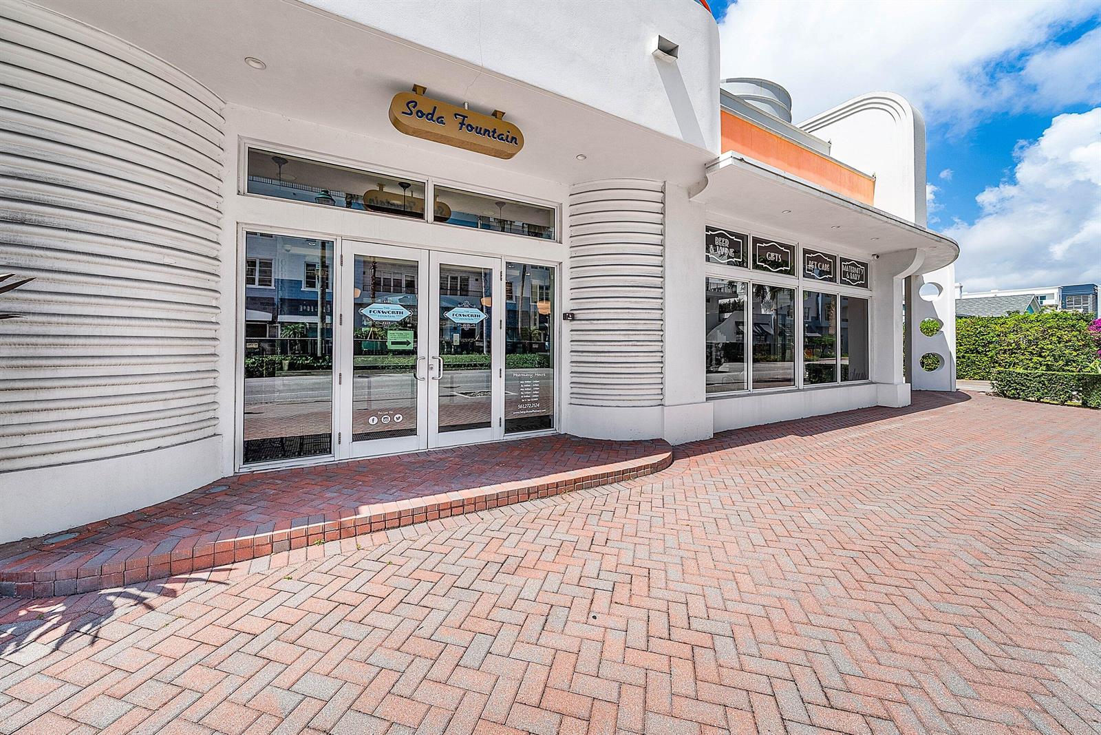 The exterior of a white commercial building features a brick walkway and soda fountain signage — 124 NE 5th Avenue, Delray Beach FL 33483, DELRAY BEACH, FL