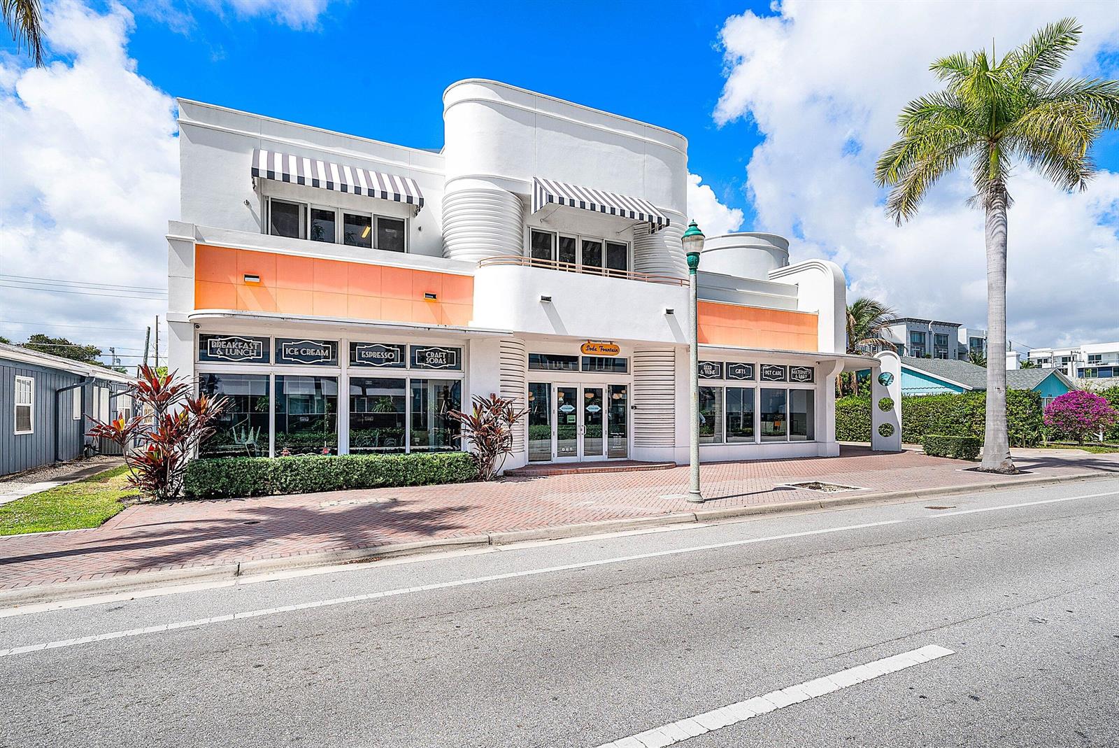 A two-story white commercial building with orange accents and striped awnings sits along a street — 124 NE 5th Avenue, Delray Beach FL 33483, DELRAY BEACH, FL