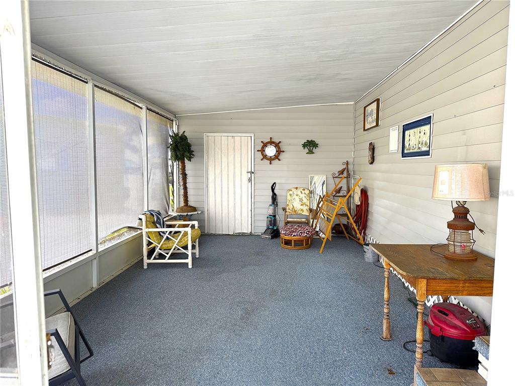 A screened-in porch features gray carpeting, light-colored siding, and various pieces of furniture — 527 BLACKBURN BOULEVARD, NORTH PORT, FL