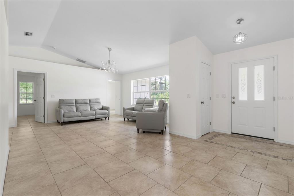 A bright living room features light tile flooring, white walls, and two gray sofas — 23 PENNFIELD LANE, PALM COAST, FL