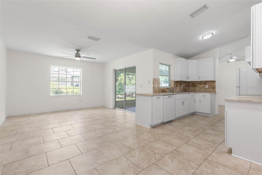 A bright kitchen with white cabinets and tile flooring opens into a spacious dining area — 23 PENNFIELD LANE, PALM COAST, FL