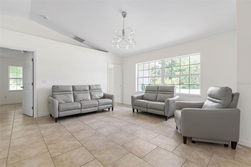 A living room features light gray leather furniture, tile flooring, and a modern chandelier — 23 PENNFIELD LANE, PALM COAST, FL