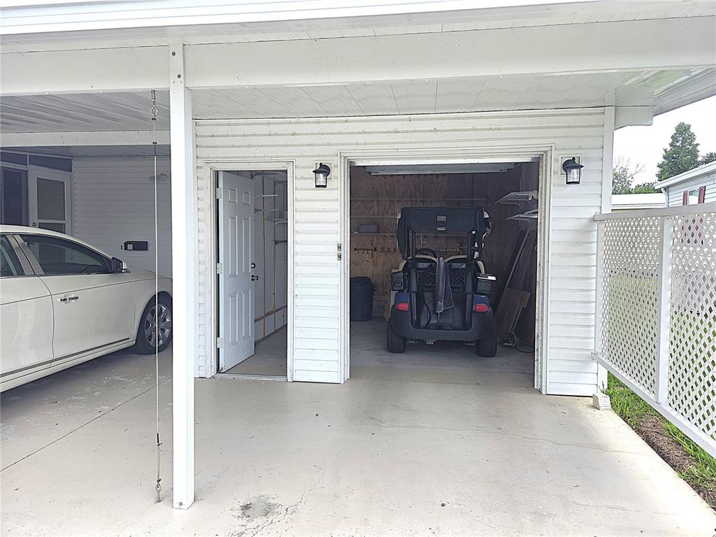 A carport features a white car, a storage room door, and a golf cart inside — 311 TOWNBRIDGE DRIVE, HAINES CITY, FL