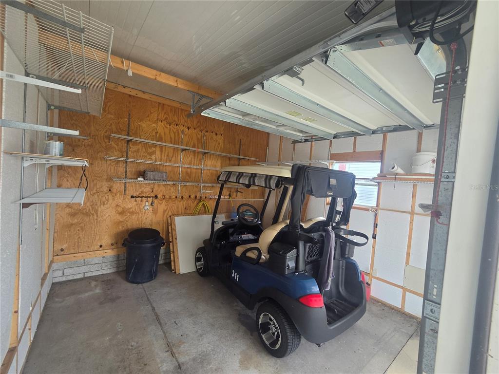 A garage with plywood walls, metal shelving, and a blue golf cart parked inside — 311 TOWNBRIDGE DRIVE, HAINES CITY, FL