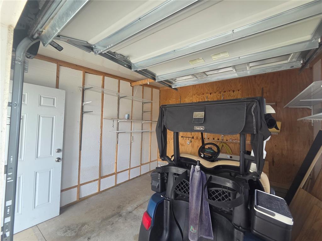 A garage interior features a golf cart, wire shelving, and exposed wall studs — 311 TOWNBRIDGE DRIVE, HAINES CITY, FL