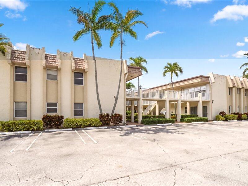 A two-story apartment building with a parking lot and palm trees under a blue sky — 600 Snug Harbor Drive # A16, Boynton Beach FL 33435, BOYNTON BEACH, FL