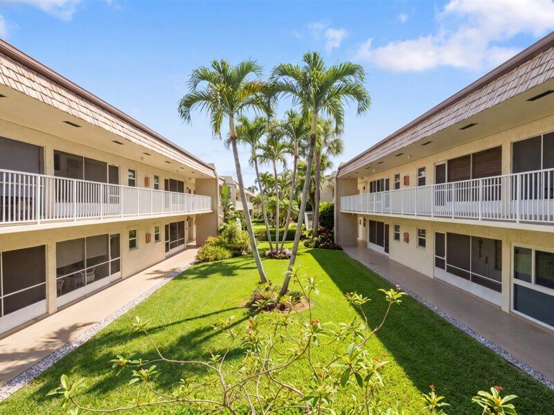 A courtyard with a green lawn and palm trees sits between two apartment buildings — 600 Snug Harbor Drive # A16, Boynton Beach FL 33435, BOYNTON BEACH, FL
