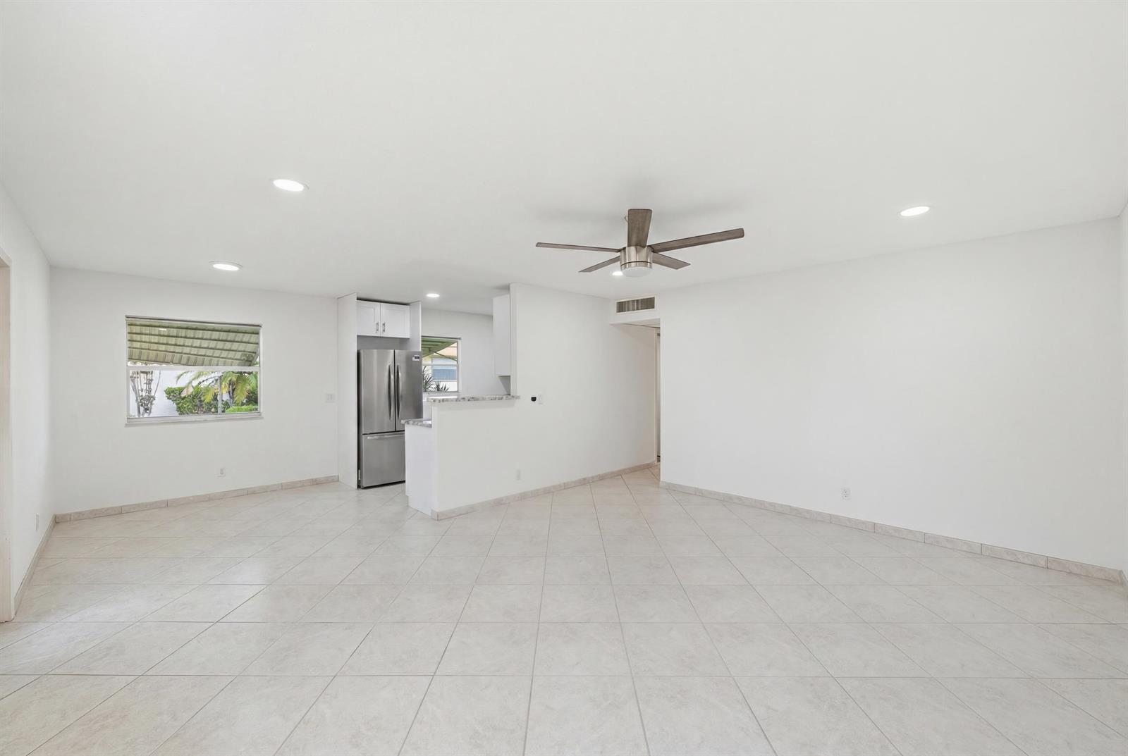 An open-concept living area features white walls, light-colored tile flooring, a ceiling fan, and a kitchen — 28 Seville 'b', Delray Beach FL 33446, DELRAY BEACH, FL