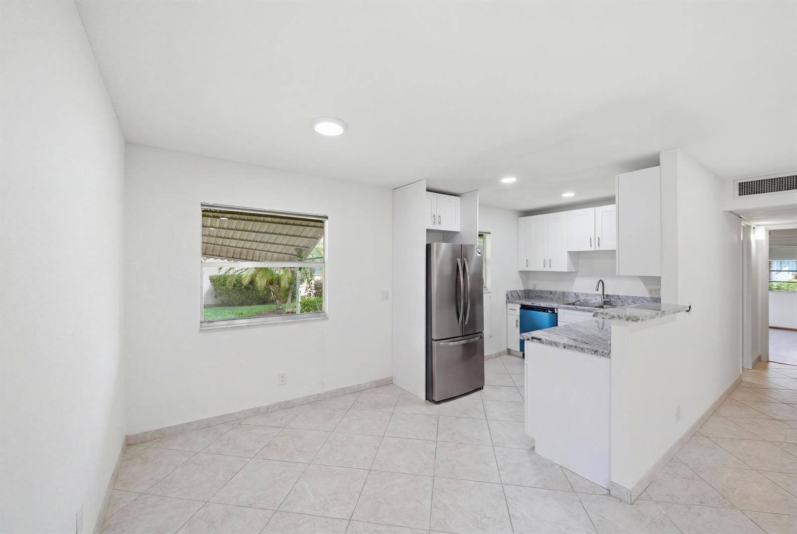 A kitchen and dining area with white cabinets, stainless steel appliances, and light tile flooring — 28 Seville 'b', Delray Beach FL 33446, DELRAY BEACH, FL