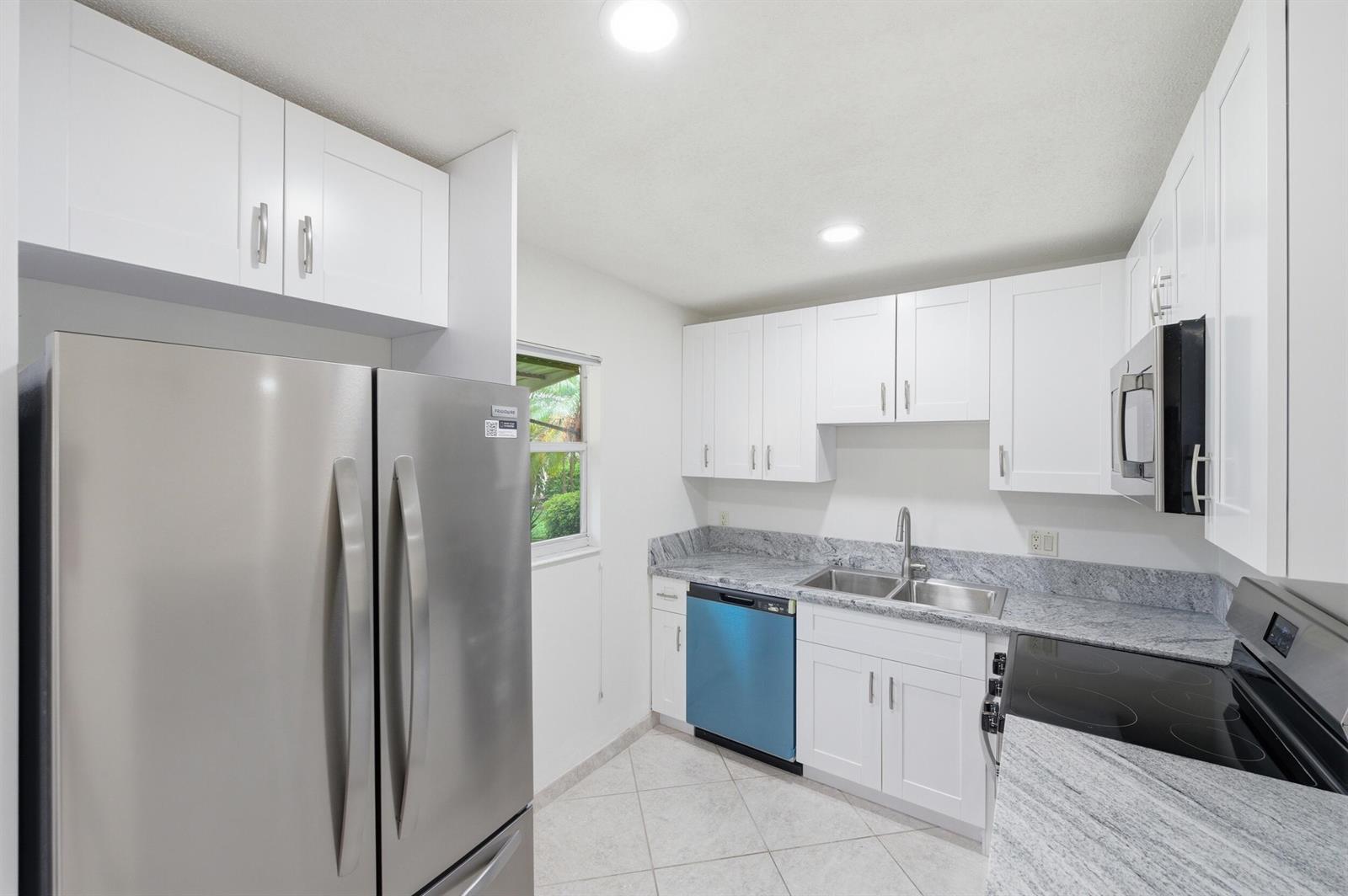 A kitchen features white cabinets, stainless steel appliances, granite countertops, and light-colored tile flooring — 28 Seville 'b', Delray Beach FL 33446, DELRAY BEACH, FL