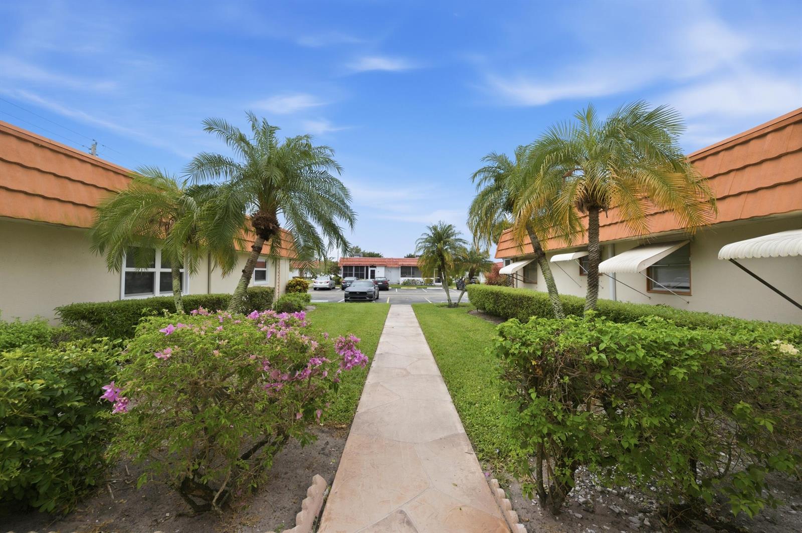 A paved walkway leads between two single-story buildings with palm trees and manicured landscaping — 28 Seville 'b', Delray Beach FL 33446, DELRAY BEACH, FL