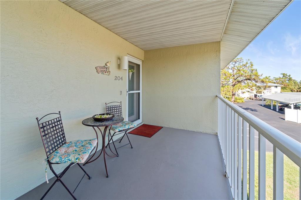 A balcony features a small bistro set, a screen door, and a view of parking — 6600 GASPARILLA PINES BOULEVARD UNIT 204, ENGLEWOOD, FL