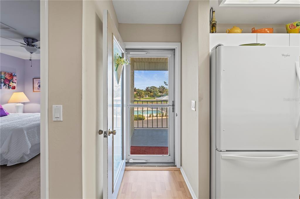 A view through an open door shows a balcony overlooking a swimming pool and trees — 6600 GASPARILLA PINES BOULEVARD UNIT 204, ENGLEWOOD, FL