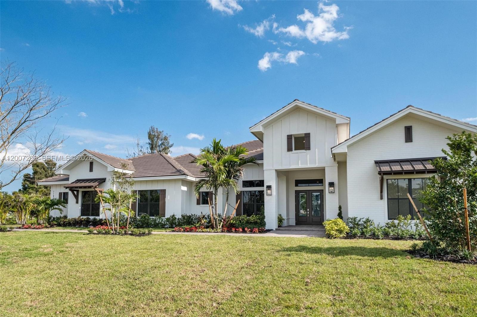 A white farmhouse-style house with a dark roof and a front lawn under a blue sky — 11900 SW 14th Pl, Davie FL 33325, DAVIE, FL