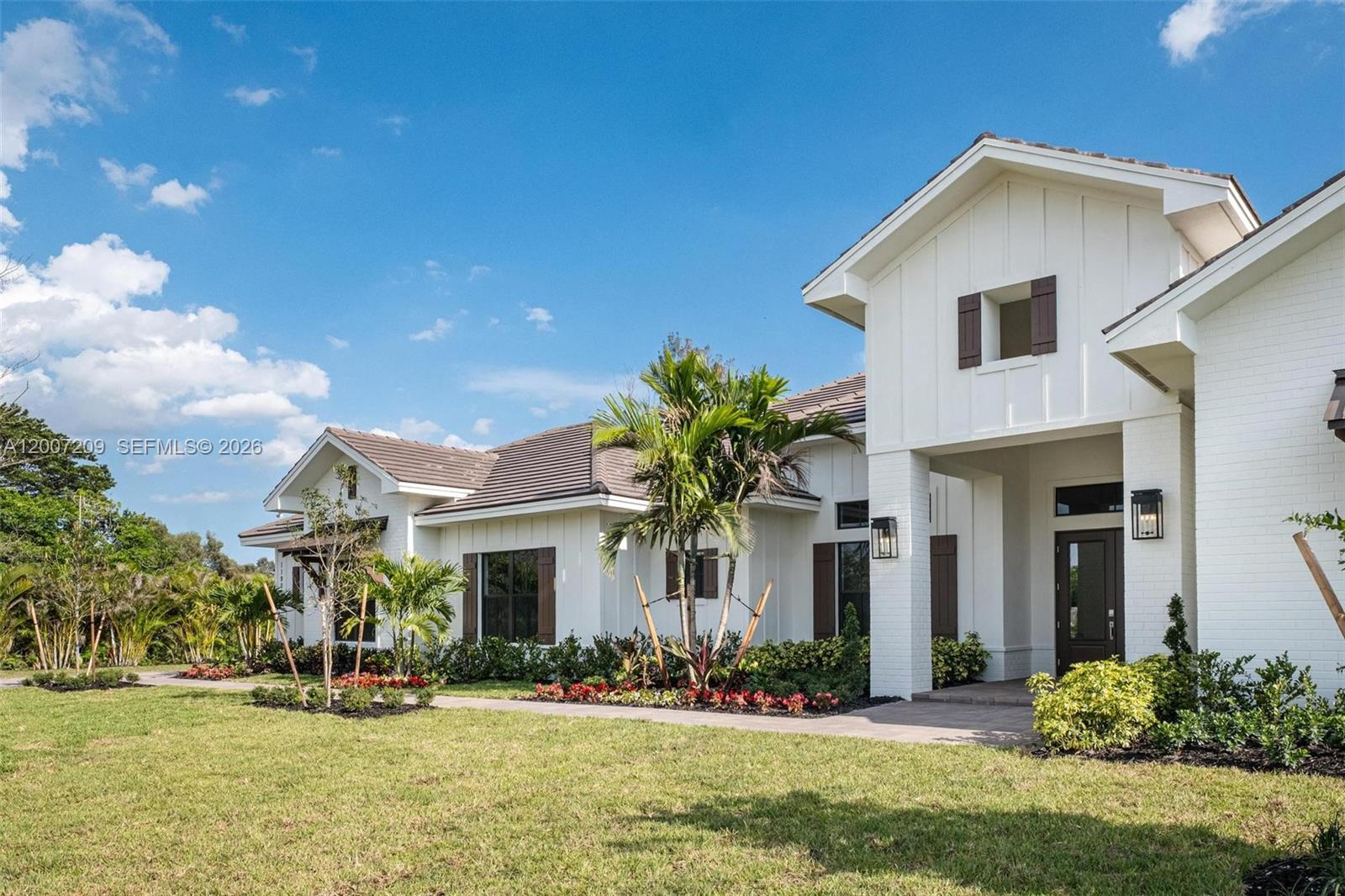 A white farmhouse-style home features a brown tiled roof, dark shutters, and landscaped front yard — 11900 SW 14th Pl, Davie FL 33325, DAVIE, FL