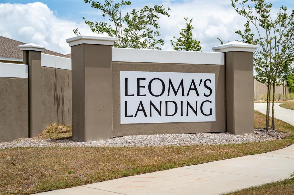 A beige stucco monument sign for Leoma's Landing stands outdoors near a concrete sidewalk — 573 BELL PRAIRIE CIRCLE, LAKE WALES, FL