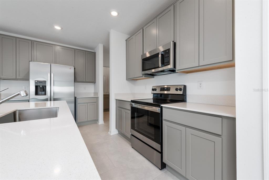 A modern kitchen features gray cabinets, stainless steel appliances, and white quartz countertops — 573 BELL PRAIRIE CIRCLE, LAKE WALES, FL