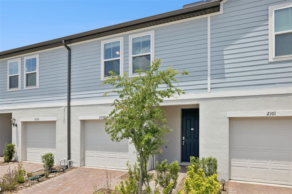 The exterior of a multi-unit townhouse features light blue siding, white stucco, and garage doors — 2097 CRAPE JASMINE LANE, ORLANDO, FL
