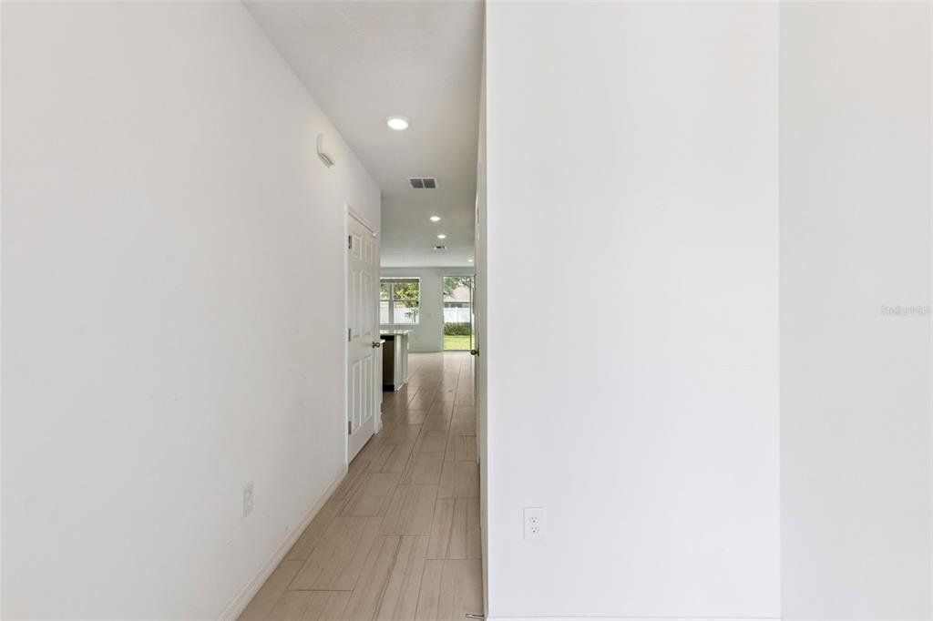 A hallway with light wood-look tile flooring leads toward an open kitchen and living area — 2097 CRAPE JASMINE LANE, ORLANDO, FL