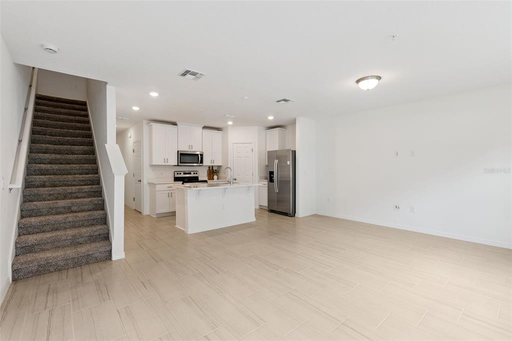 An open-concept living area features a carpeted staircase, white kitchen cabinetry, and light tile flooring — 2097 CRAPE JASMINE LANE, ORLANDO, FL