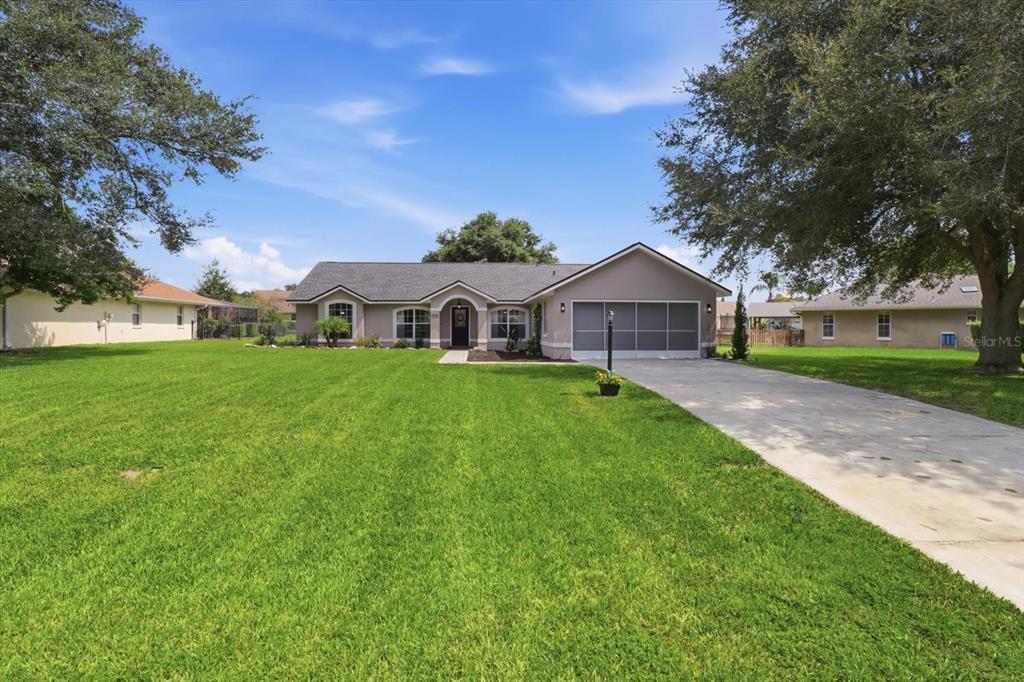 A single-story house with a gray roof, tan stucco exterior, and a large front lawn — 9285 COUNTY ROAD 125B, WILDWOOD, FL