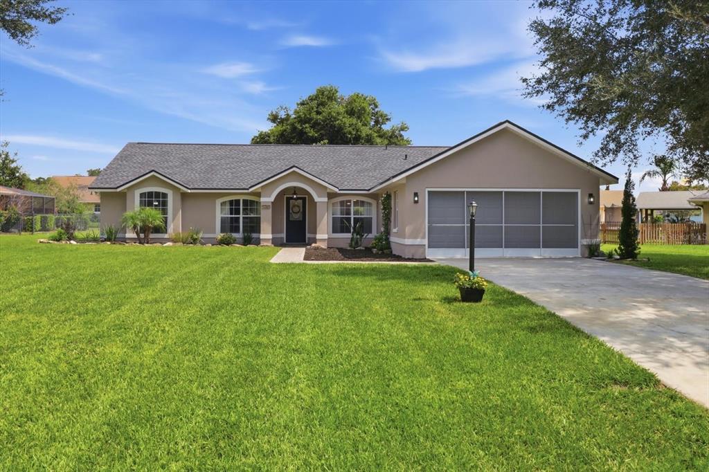 A single-story house with a beige exterior, a gray shingled roof, and a screened garage door — 9285 COUNTY ROAD 125B, WILDWOOD, FL