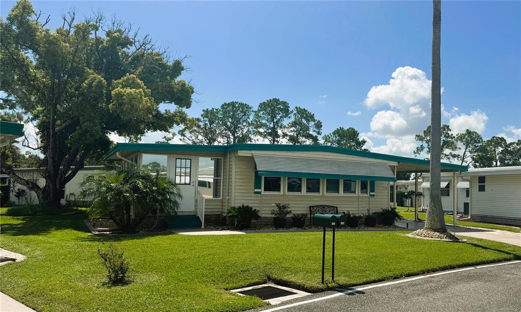 A single-story mobile home with beige siding, teal trim, and a metal awning over windows — 136 DOGWOOD TRAIL, LEESBURG, FL