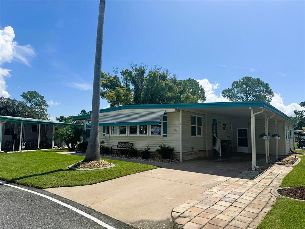 A single-story manufactured home features light siding, a metal awning, and an attached carport — 136 DOGWOOD TRAIL, LEESBURG, FL