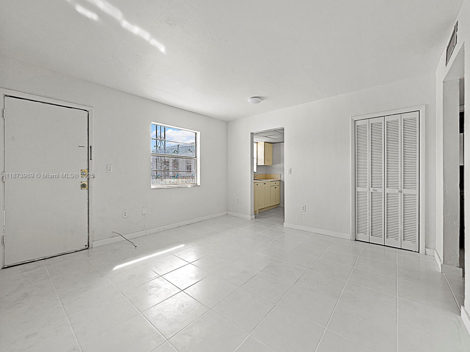 An empty room features white tile flooring, white walls, a window, and a closet door — 10305 SW 40th St # 0, Miami FL 33165, MIAMI, FL