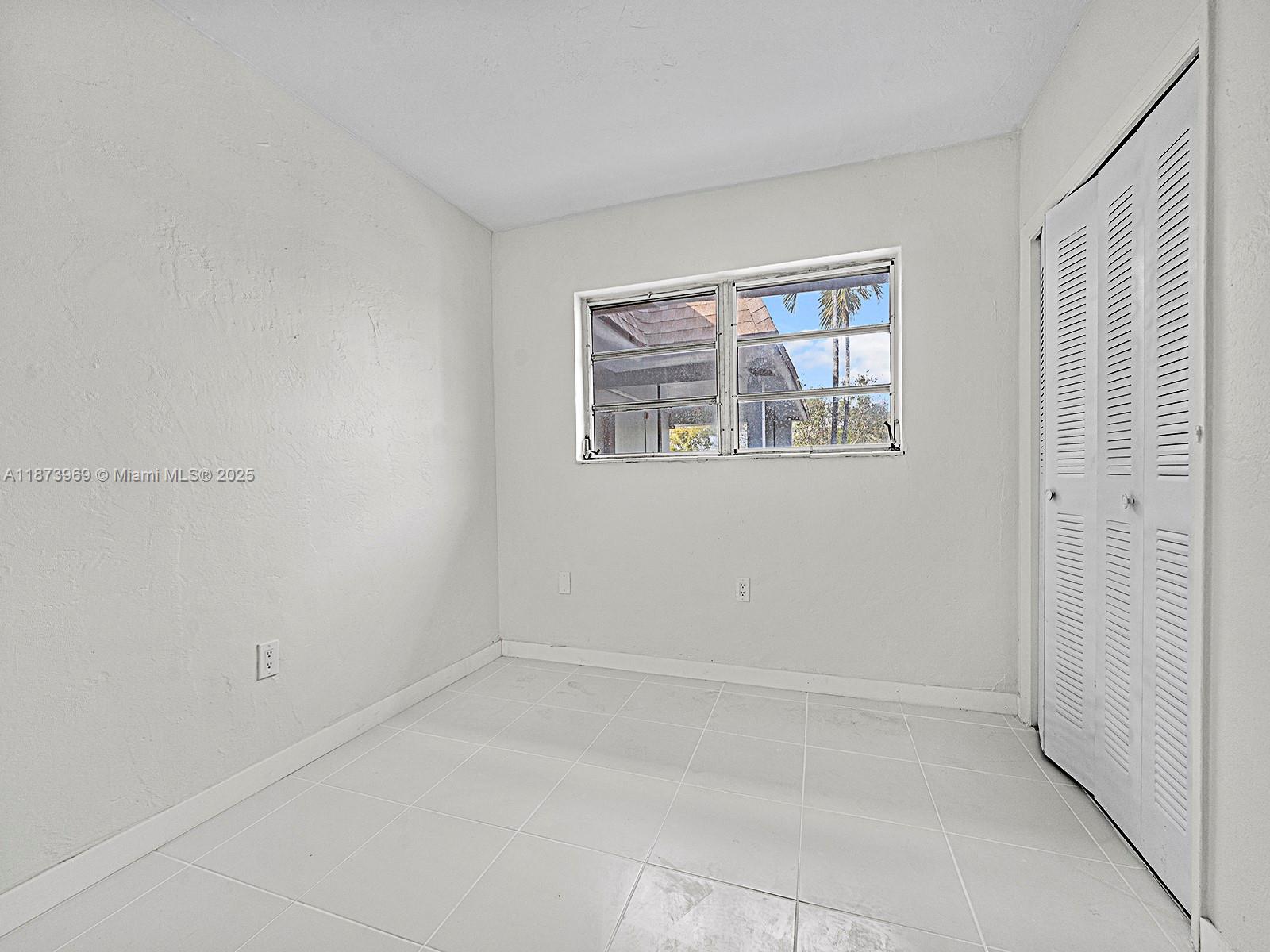 A small, empty room features white walls, tiled flooring, a window, and a louvered closet — 10305 SW 40th St # 0, Miami FL 33165, MIAMI, FL