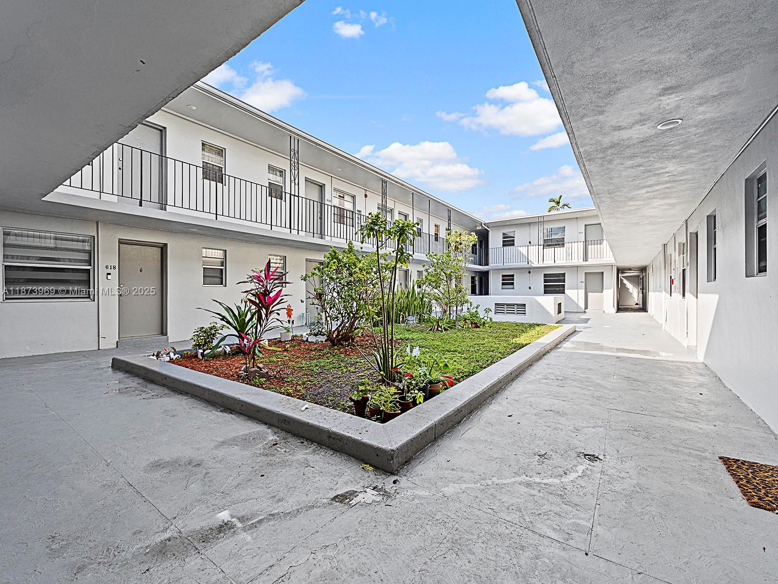 An open-air courtyard features a central garden bed surrounded by a concrete walkway and balconies — 10305 SW 40th St # 0, Miami FL 33165, MIAMI, FL