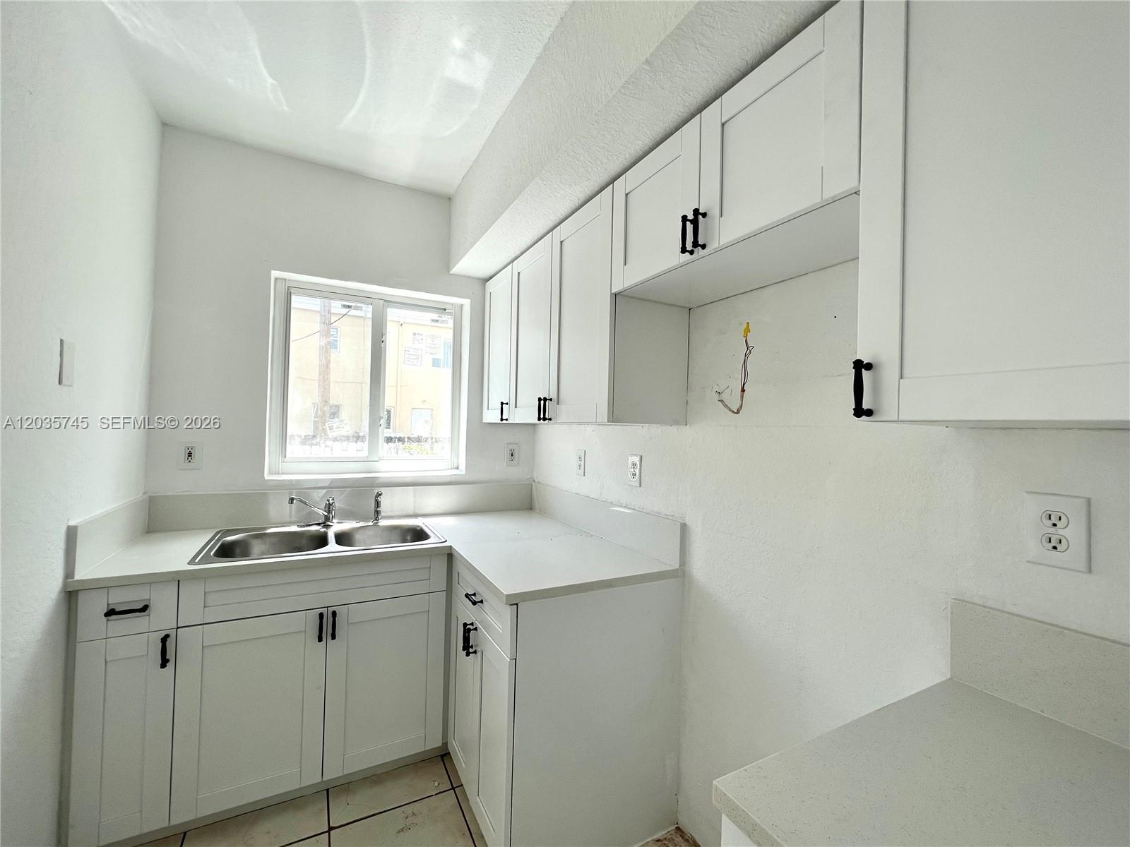 A white kitchen features a double-basin sink, white cabinets, and light-colored countertops — 444 NW 84th St # 444, Miami FL 33150, MIAMI, FL