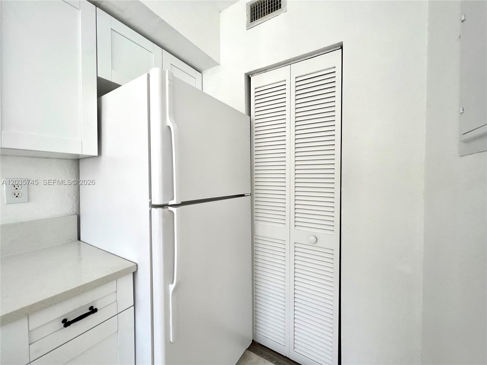 A white refrigerator stands next to a louvered closet door in a white kitchen — 444 NW 84th St # 444, Miami FL 33150, MIAMI, FL