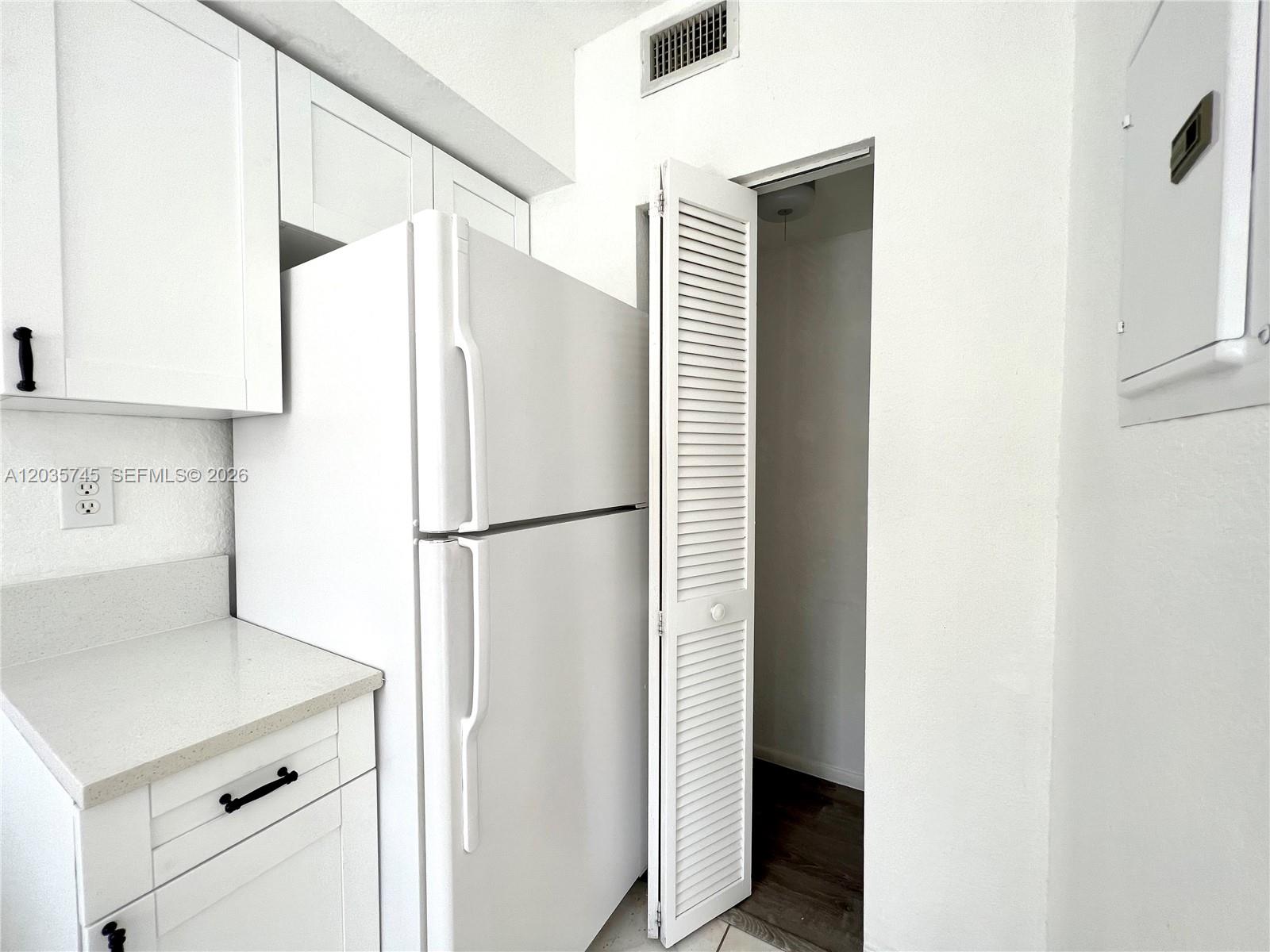 A white refrigerator stands next to a louvered closet door in a white kitchen — 444 NW 84th St # 444, Miami FL 33150, MIAMI, FL