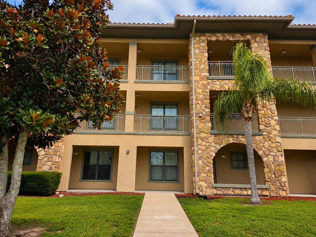 A three-story apartment building with tan stucco walls, stone accents, and balconies — 901 CHARO PARKWAY UNIT 714, DAVENPORT, FL